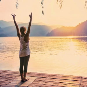Yoga Sun Salutation. Young woman doing yoga by the lake. Toned image