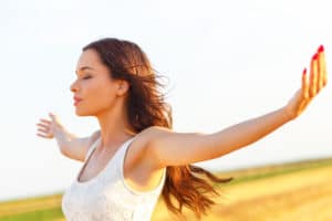 Portrait of beautiful young woman in field with her arms outstretched.